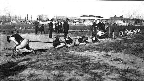 An old photo capturing the impressive display of willpower as a group of people exude a force of greatness by pulling a rope together.